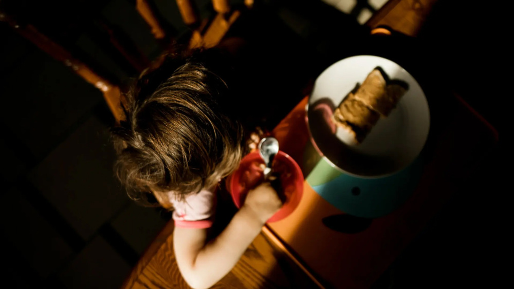 An overhead photograph of a child eating breakfast at a table.